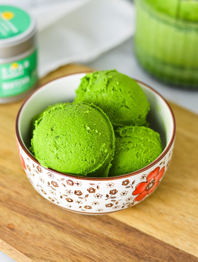 A small bowl filled with bright green Ninja Creami Matcha Ice Cream, with green tea powder in the background.