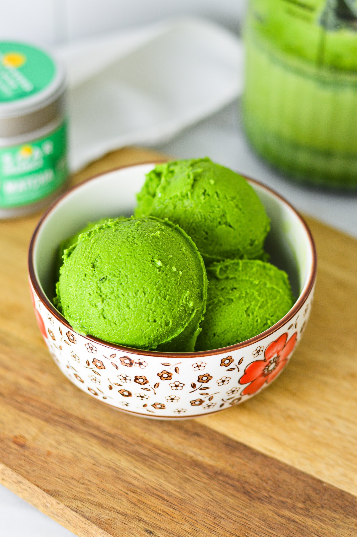 A small bowl filled with bright green Ninja Creami Matcha Ice Cream, with green tea powder in the background.