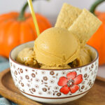 A gold spoon sticking into a bowl of Ninja Creami Vegan Pumpkin Pie Protein Ice Cream with some graham cracker cookies sticking out of the smooth ice cream.