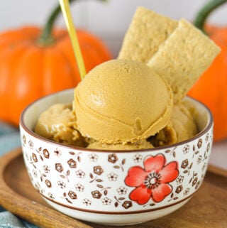 A gold spoon sticking into a bowl of Ninja Creami Vegan Pumpkin Pie Protein Ice Cream with some graham cracker cookies sticking out of the smooth ice cream.