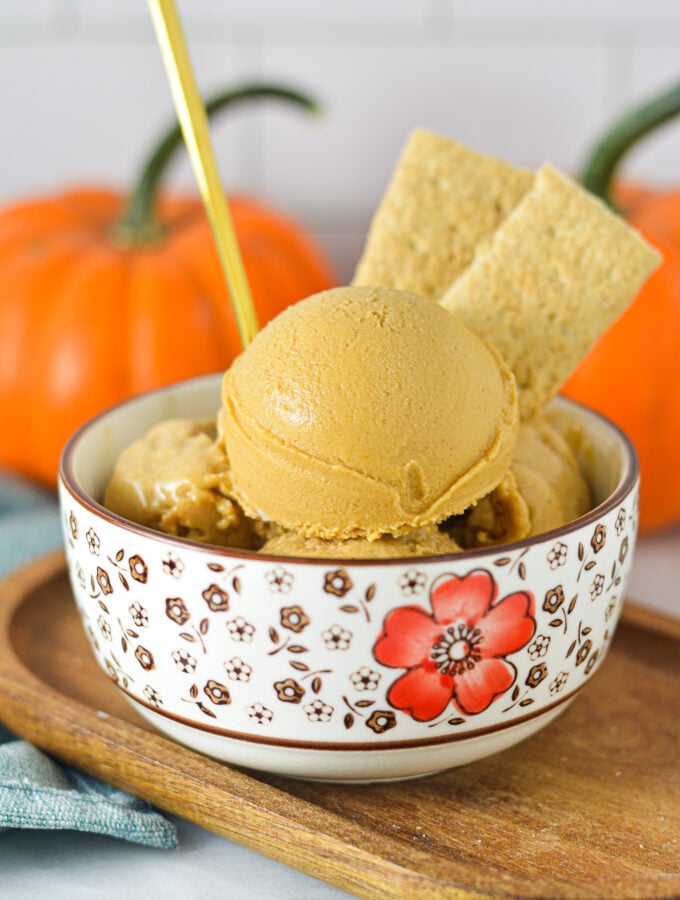 A gold spoon sticking into a bowl of Ninja Creami Vegan Pumpkin Pie Protein Ice Cream with some graham cracker cookies sticking out of the smooth ice cream.