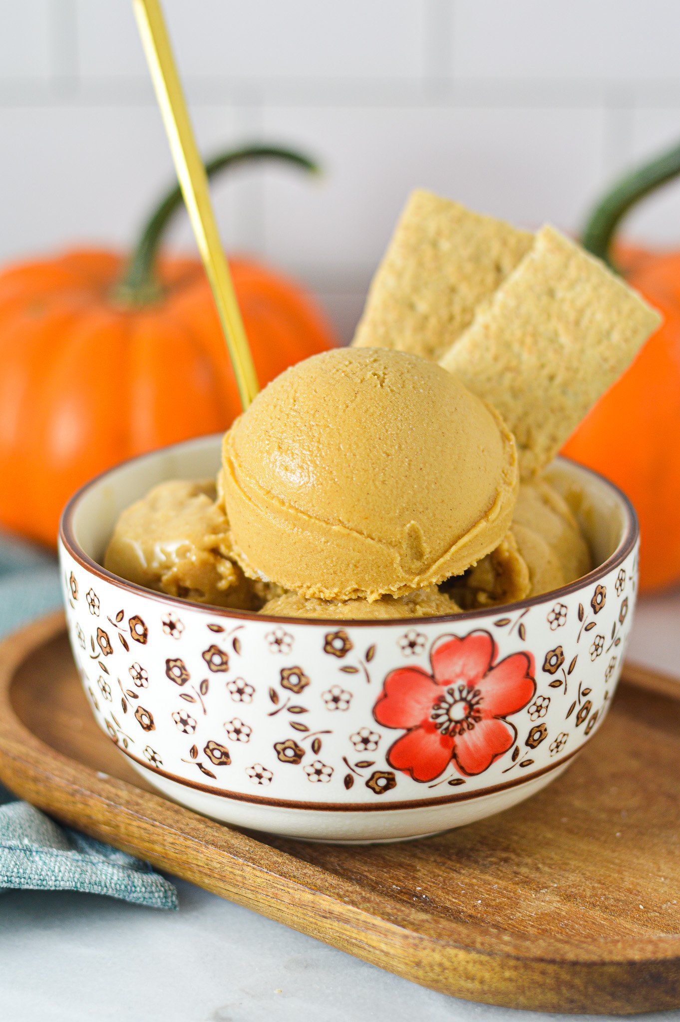 A gold spoon sticking into a bowl of Ninja Creami Vegan Pumpkin Pie Protein Ice Cream with some graham cracker cookies sticking out of the smooth ice cream.