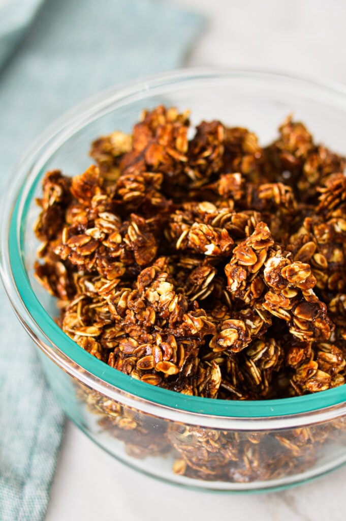 A glass container filled with large clumps of Nutella Granola.