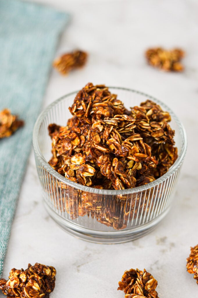 A small bowl filled with Nutella Granola on a granite surface, with more clumps of homemade granola in the background.
