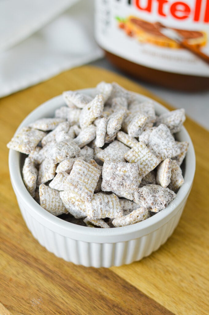A bowl of homemade Nutella Puppy Chow, showing bite-sized cereal pieces dusted with powdered sugar.