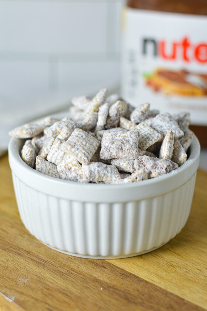 A bowl of Nutella Puppy Chow with a jar of Nutella in the background.