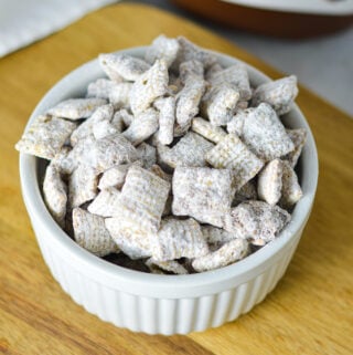 A ramekin filled with Nutella Puppy Chow, with each Chex cereal piece coated in Nutella chocolate and dusted with icing sugar.