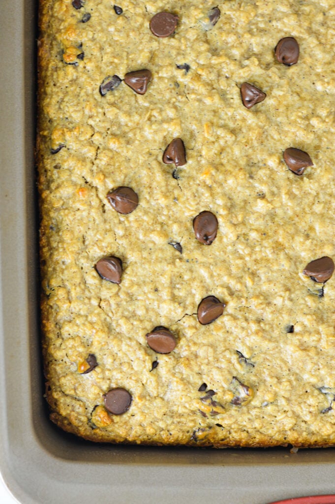 A square baking pan filled with freshly baked Peanut Butter Chocolate Chip Baked Oatmeal, studded with melted chocolate chips in the hearty baked oatmeal.