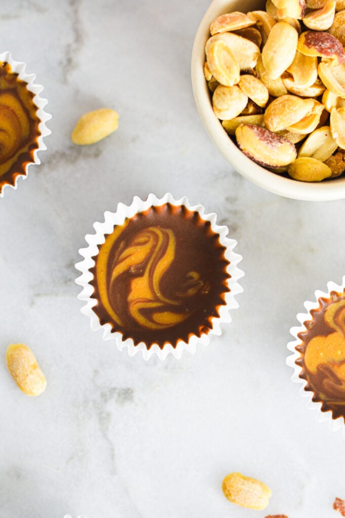 Mini Peanut Butter Swirl Nutella Cups in mini paper liners, with some roasted peanuts in a small bowl in the background.
