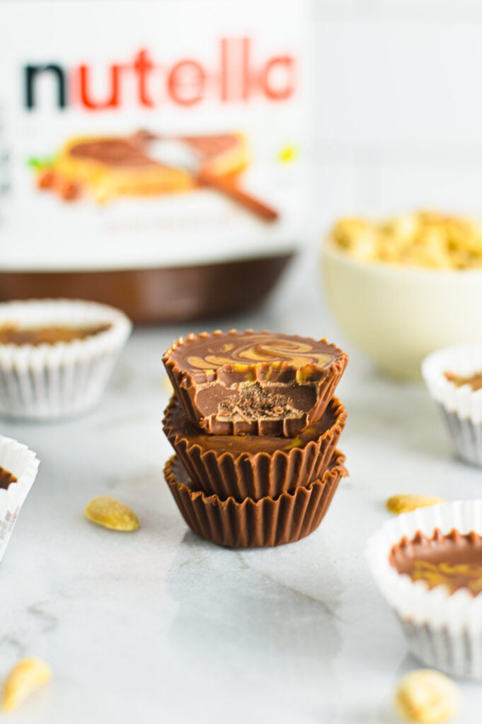 A stack of Peanut Butter Swirl Nutella Cups on a granite surface with a bite taken out of the top Nutella cup showing the creamy chocolate base.