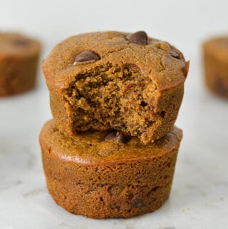 A stack of golden brown Protein Mocha Chocolate Chip Muffins with a bite taken out of the top muffin showing its soft texture.