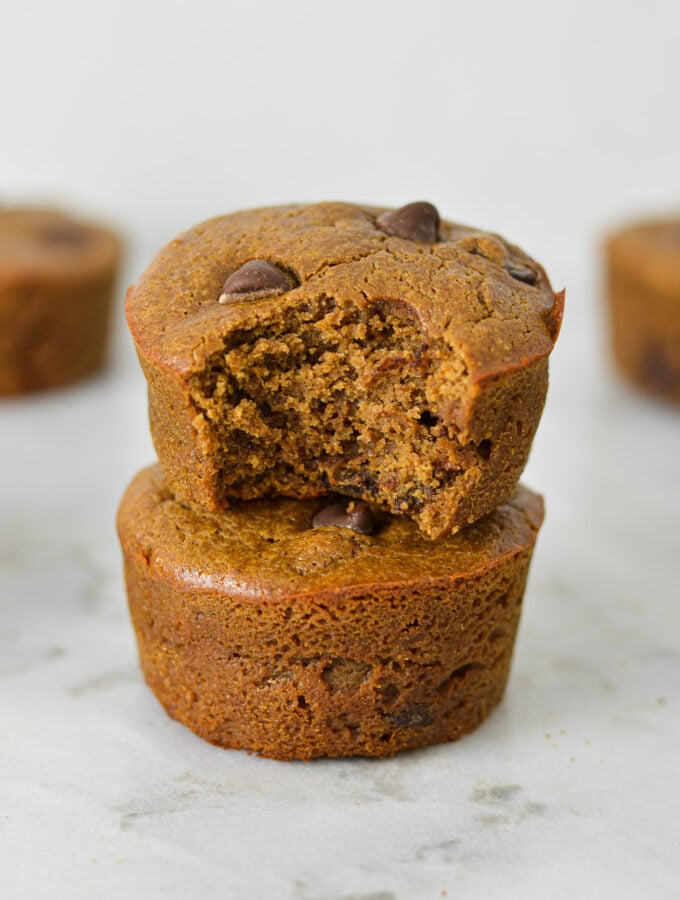 A stack of golden brown Protein Mocha Chocolate Chip Muffins with a bite taken out of the top muffin showing its soft texture.