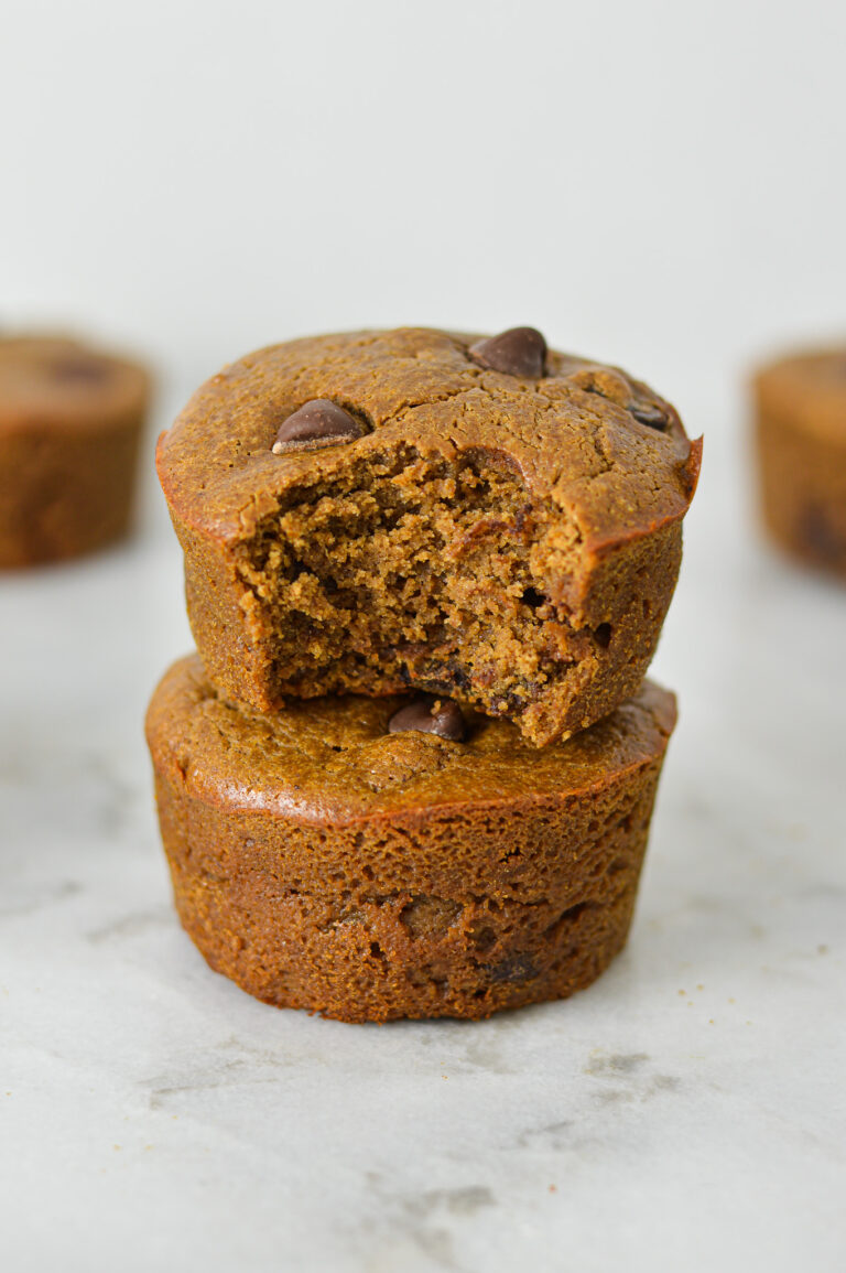 A stack of golden brown Protein Mocha Chocolate Chip Muffins with a bite taken out of the top muffin showing its soft texture.