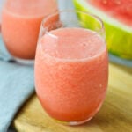 A vibrant pink Frozen Watermelon Daiquiri served in a glass with a sliced watermelon in the background.