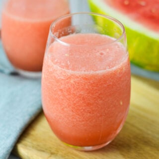 A vibrant pink Frozen Watermelon Daiquiri served in a glass with a sliced watermelon in the background.