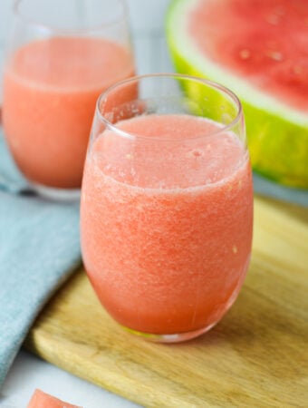 A vibrant pink Frozen Watermelon Daiquiri served in a glass with a sliced watermelon in the background.