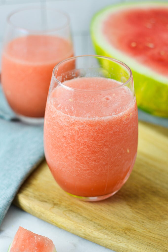 A vibrant pink Frozen Watermelon Daiquiri served in a glass with a sliced watermelon in the background.