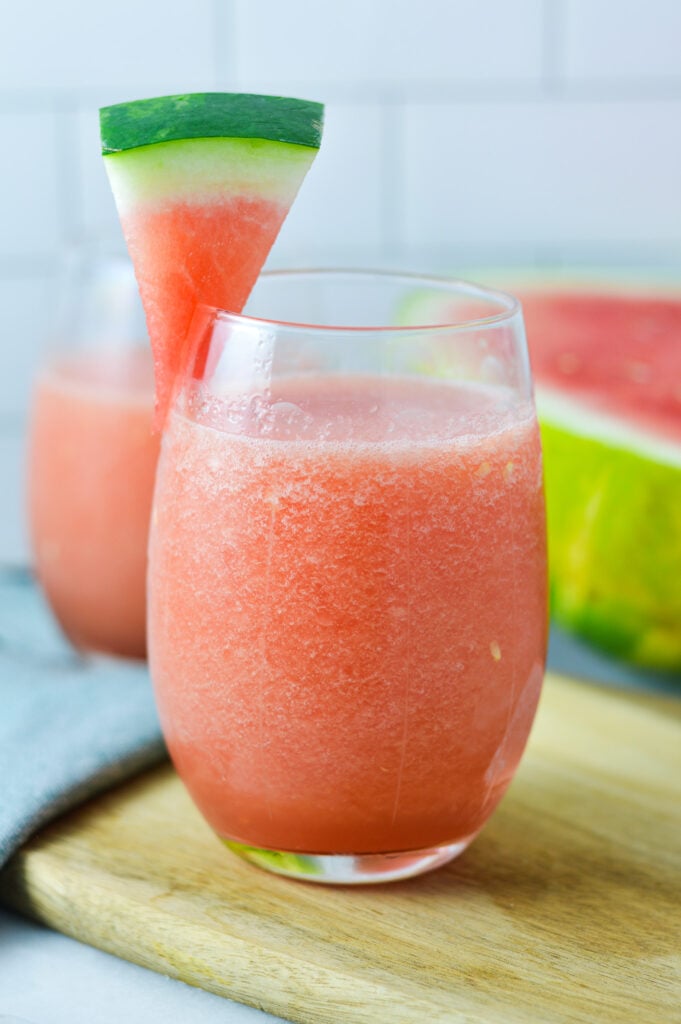 Two glasses of Frozen Watermelon Daiquiri on a wooden surface, garnished with a small watermelon wedge.