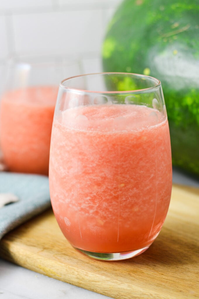 Two glass cups of Frozen Watermelon Daiquiri, served on a wooden cutting board with a fresh watermelon in the background.