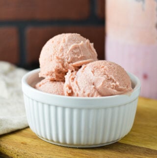 A white ramekin filled with Ninja Creami Cherry Ice Cream with a Ninja Creami container filled with the creamy ice cream in the background.