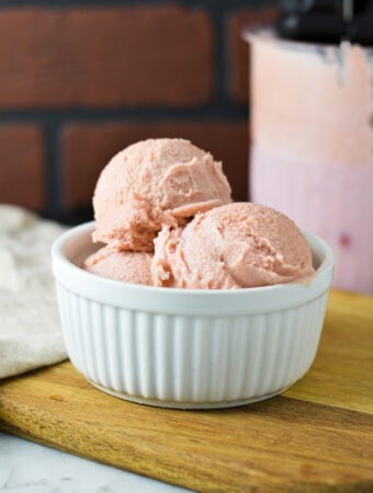 A white ramekin filled with Ninja Creami Cherry Ice Cream with a Ninja Creami container filled with the creamy ice cream in the background.