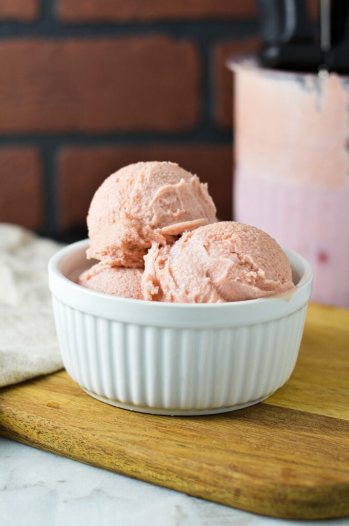 A white ramekin filled with Ninja Creami Cherry Ice Cream with a Ninja Creami container filled with the creamy ice cream in the background.