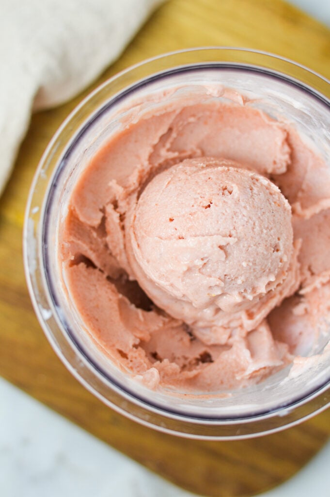 A Ninja Creami pint container filled with creamy cherry ice cream, with a scoop on top showing its smooth texture.