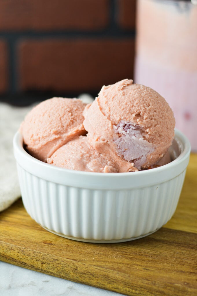 A small bowl filled with Ninja Creami Cherry Ice Cream, with some cherry pieces showing throughout the pink ice cream.