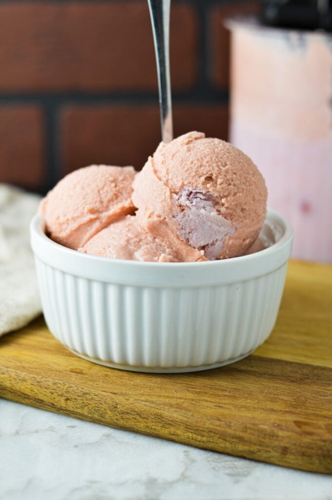 A small white bowl with some Cherry ice cream made from a Ninja Creami machine on a wooden surface, with a small spoon stuck into the creamy ice cream.