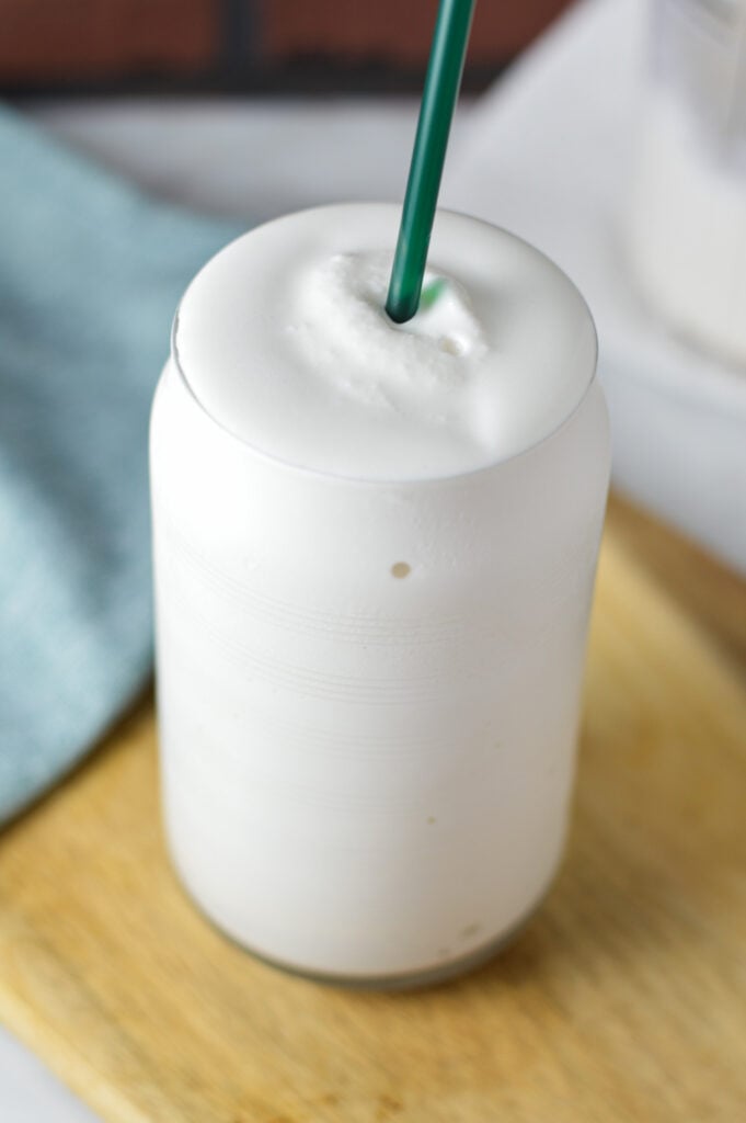 A tall glass filled with Ninja Creami Frozen White Hot Chocolate, with a green straw sticking out of the creamy drink.
