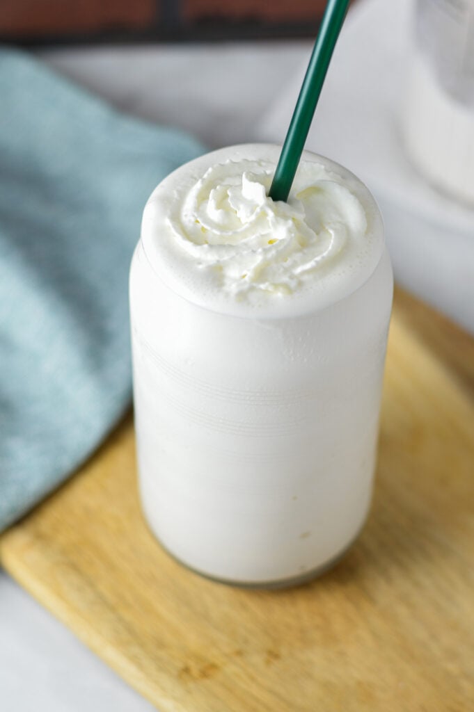 Creamy frozen white hot chocolate made in the Ninja Creami machine, topped with whipped cream and served with a green straw.
