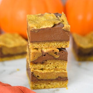 Gooey Pumpkin Nutella Bars stacked on a granite surface, showing layers of golden pumpkin batter swirled with rich Nutella spread.