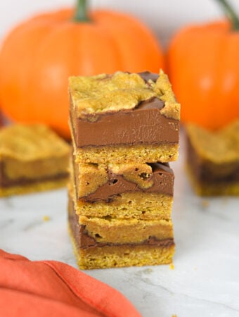 Gooey Pumpkin Nutella Bars stacked on a granite surface, showing layers of golden pumpkin batter swirled with rich Nutella spread.