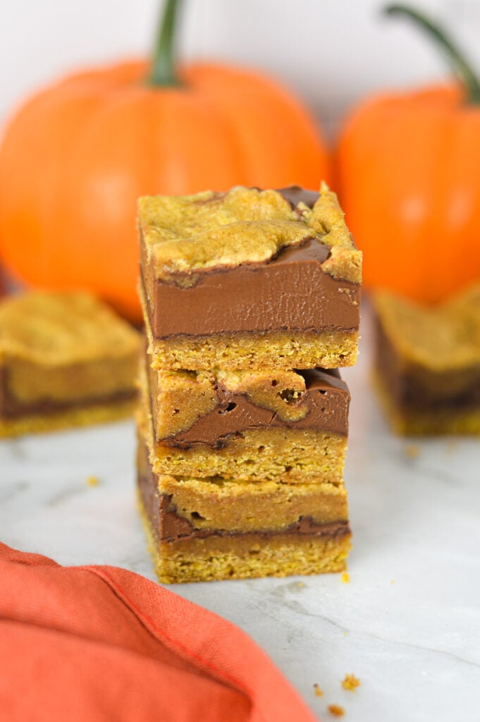 Gooey Pumpkin Nutella Bars stacked on a granite surface, showing layers of golden pumpkin batter swirled with rich Nutella spread.