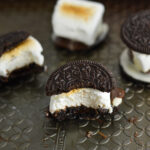 S'moreos on a baking sheet, with toasted marshmallows sandwiched between two Oreo cookies, with melted chocolate coming out of the sides.