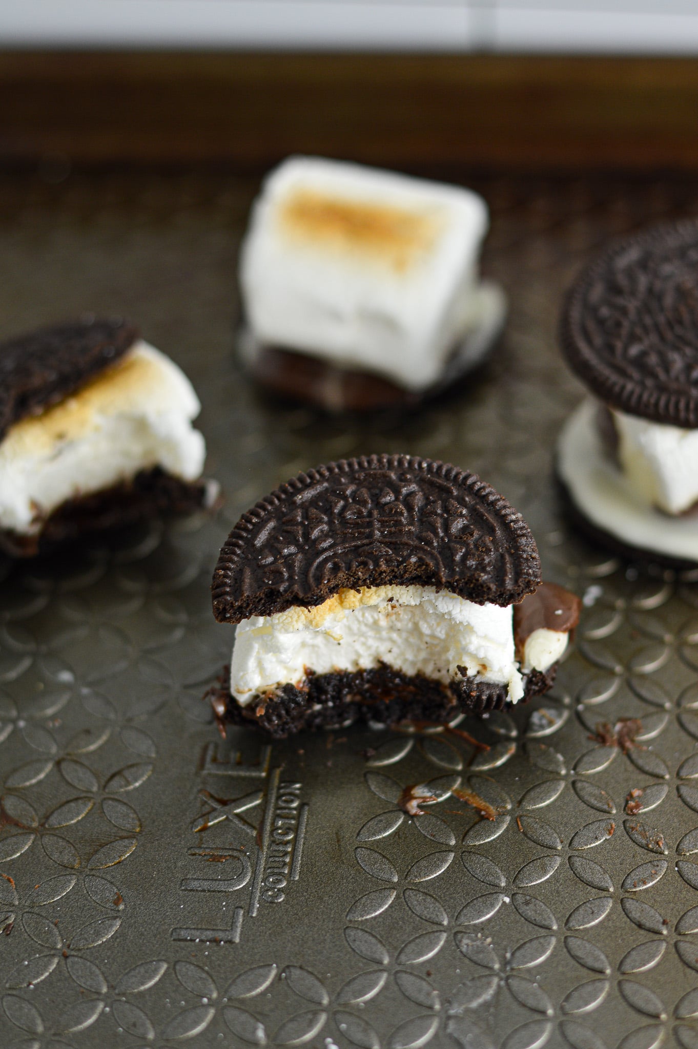 S'moreos on a baking sheet, with toasted marshmallows sandwiched between two Oreo cookies, with melted chocolate coming out of the sides.