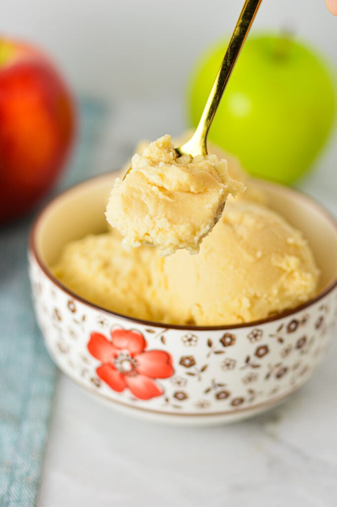 A small spoon taking a scoop of Ninja Creami Caramel Apple Sorbet, with Gala and Granny Smith apples in the background.