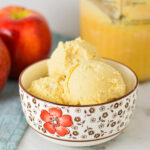 A small bowl filled with scoops of homemade Ninja Creami Caramel Apple Sorbet, with Gala apples in the background.