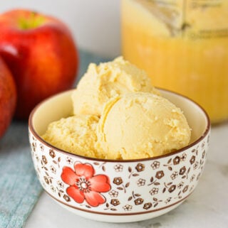 A small bowl filled with scoops of homemade Ninja Creami Caramel Apple Sorbet, with Gala apples in the background.