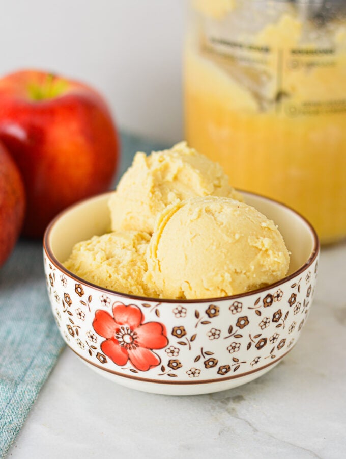 A small bowl filled with scoops of homemade Ninja Creami Caramel Apple Sorbet, with Gala apples in the background.