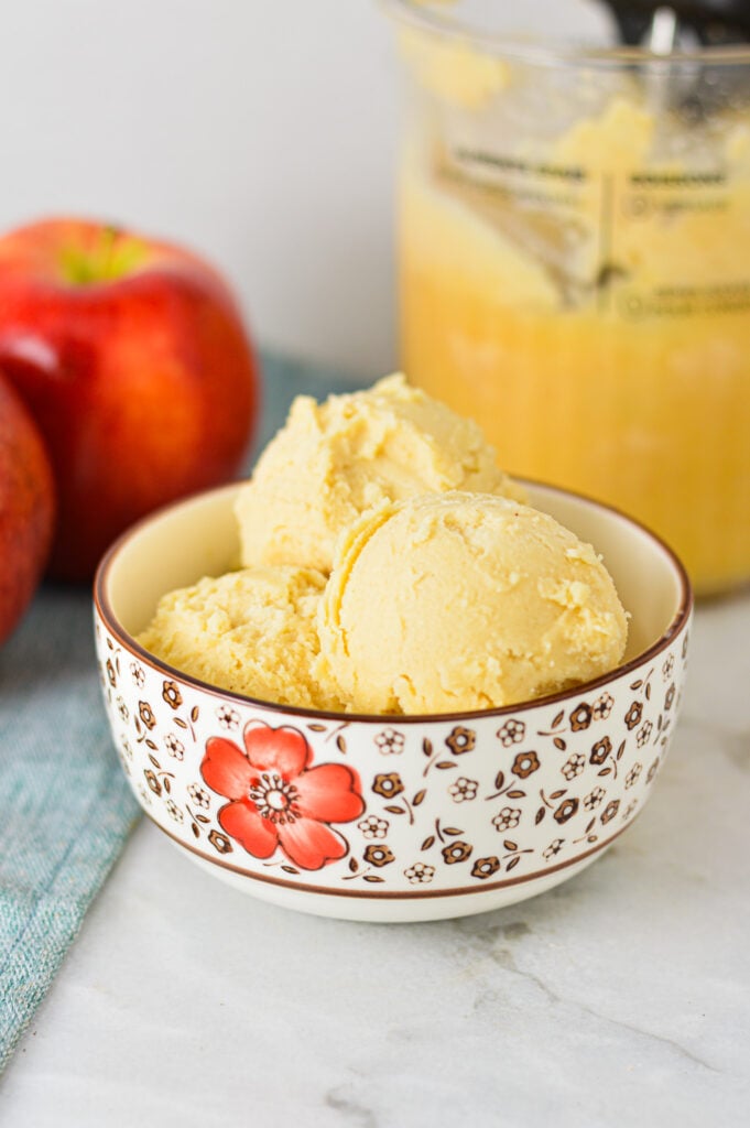 A small bowl filled with scoops of homemade Ninja Creami Caramel Apple Sorbet, with Gala apples in the background.