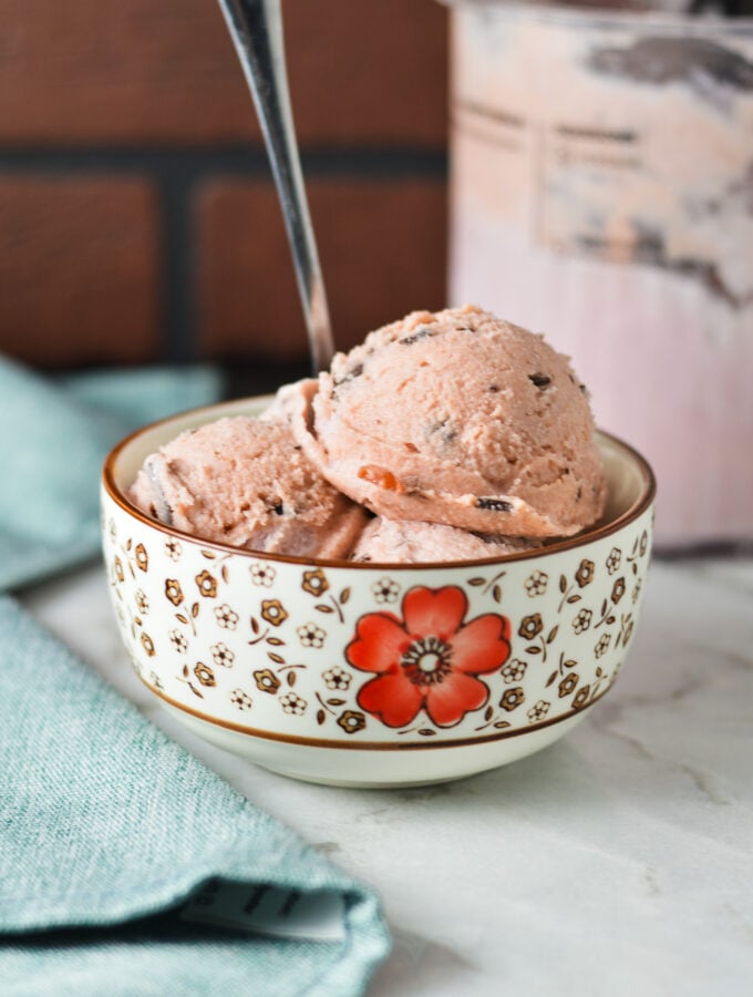 A small bowl filled with Ninja Creami Cherry Chocolate Chunk Ice Cream, with a spoon sticking out of the creamy ice cream.