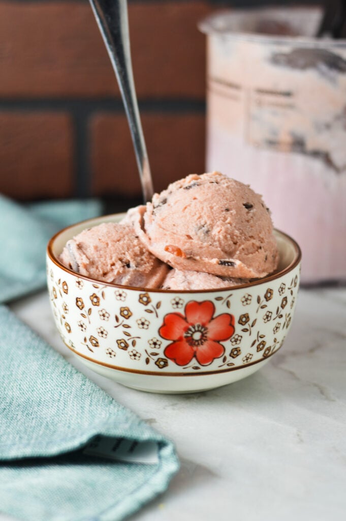 A small bowl filled with Ninja Creami Cherry Chocolate Chunk Ice Cream, with a spoon sticking out of the creamy ice cream.