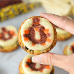 A hand holding a Thanksgiving Chocolate Chip Sugar Cookie Cups, with some decorative corn in the background giving it a holiday feel.