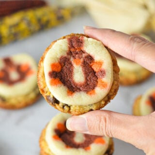 A hand holding a Thanksgiving Chocolate Chip Sugar Cookie Cups, with some decorative corn in the background giving it a holiday feel.