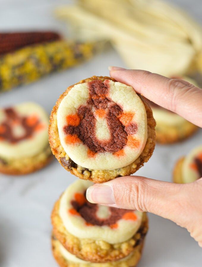 A hand holding a Thanksgiving Chocolate Chip Sugar Cookie Cups, with some decorative corn in the background giving it a holiday feel.
