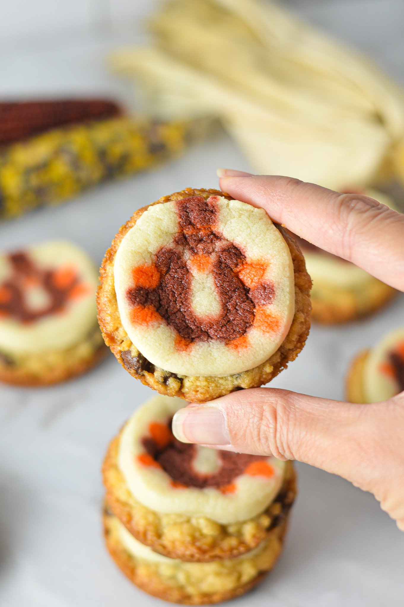 A hand holding a Thanksgiving Chocolate Chip Sugar Cookie Cups, with some decorative corn in the background giving it a holiday feel.