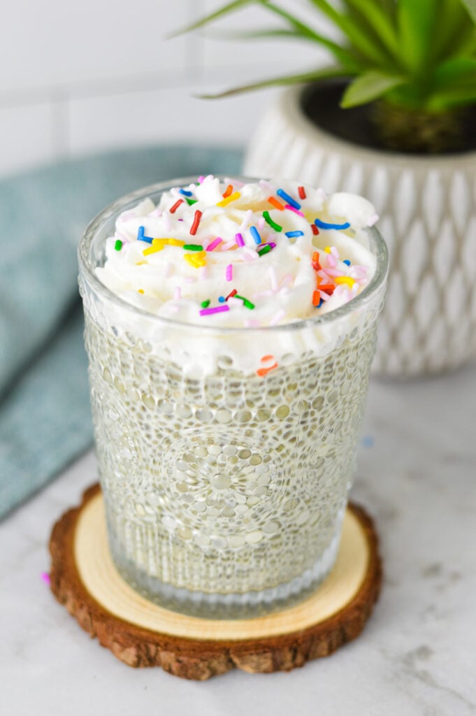 A small glass filled with Birthday Cake Chia Pudding, topped with whipped cream and rainbow sprinkles.