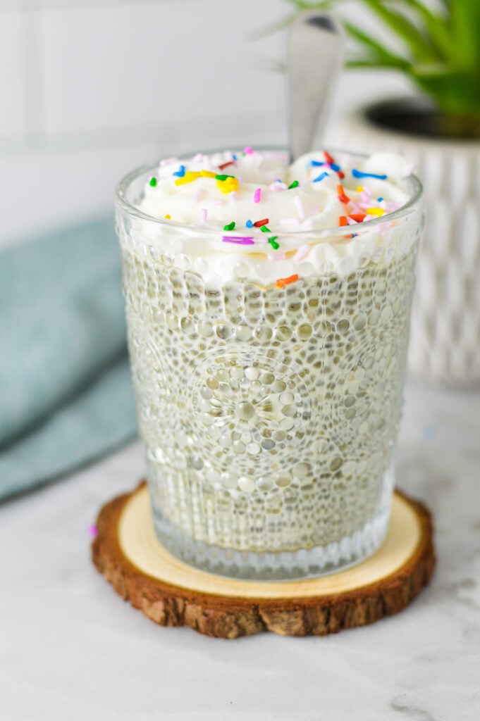 A small cup filled with Birthday Cake Chia Pudding, topped with creamy whipped cream and colorful sprinkles.