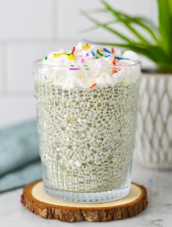 A glass cup filled with Birthday Cake Chia Pudding, topped with whipped cream and candy sprinkles.